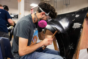 A student hammering car parts in class.