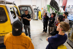 An instructor pointing to car parts to a group of students during class at Crockett high school (ACC South Austin campus.)