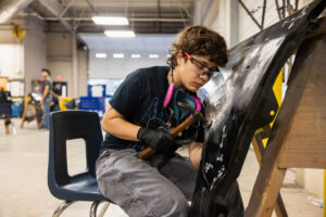 A student hammering car parts in class.